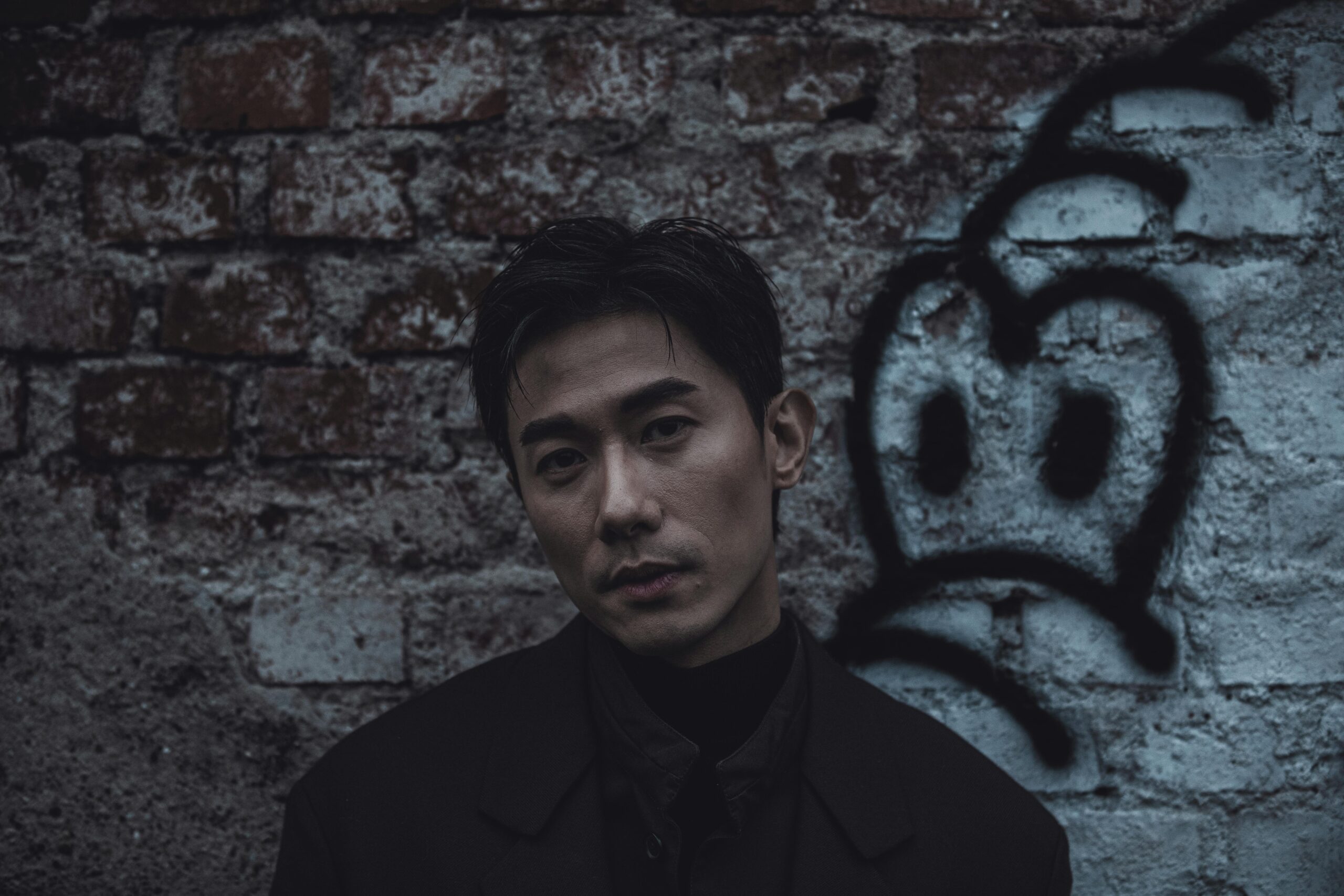 Dark and dramatic portrait of a man in front of a graffiti brick wall.