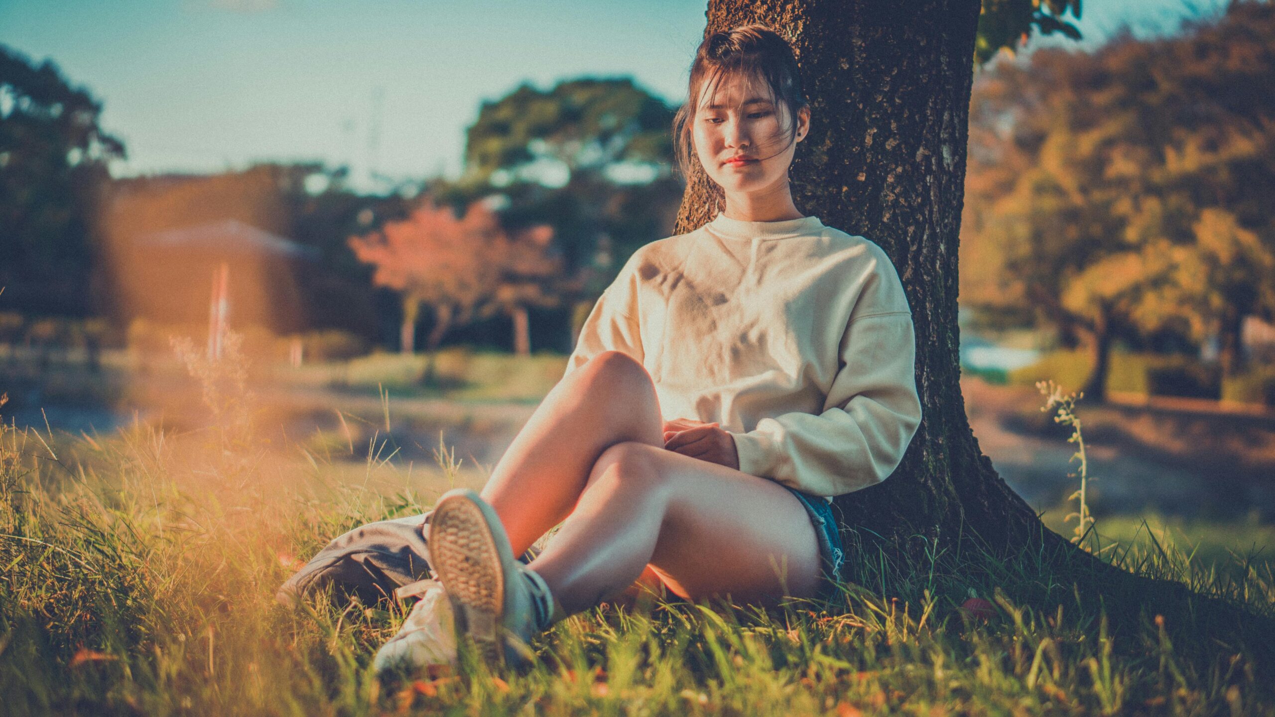 A serene moment captured as a young woman sits peacefully under a tree enjoying the outdoors.