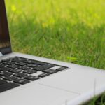 Silver laptop computer on vibrant green grass depicting remote work outdoors in summer.