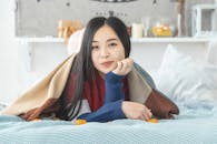 Young woman relaxing indoors, wrapped in a cozy blanket on bed. Perfect for lifestyle and relaxation themes.